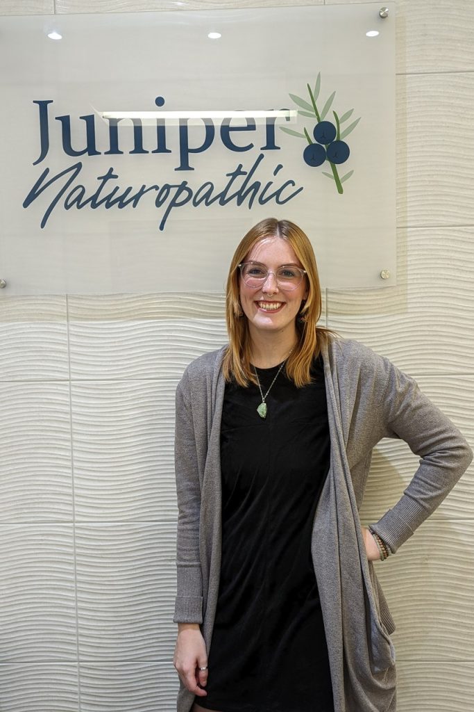 Taylor Rix standing infront of Juniper Naturopathic Sign at clinic