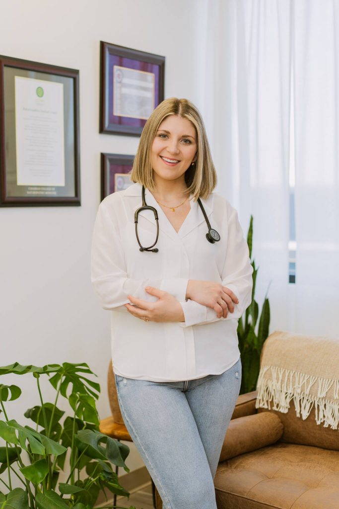 dr. anna garber naturopathic doctor standing against white wall with framed diplomas in white dress shirt and stethoscope headshot