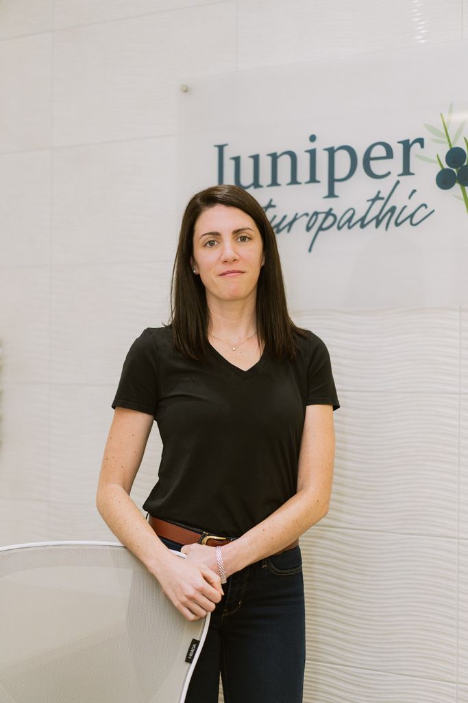 juniper naturopathic clinic administraative assistant christina tuinema standing infront of neutral white background in front of clinic signage