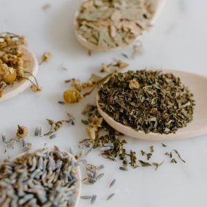 wooden spoonfuls of dried herbs on white table